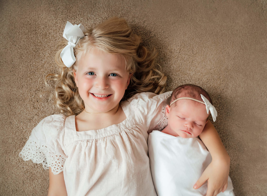 big sister posing with her new baby sister during in home newborn session 