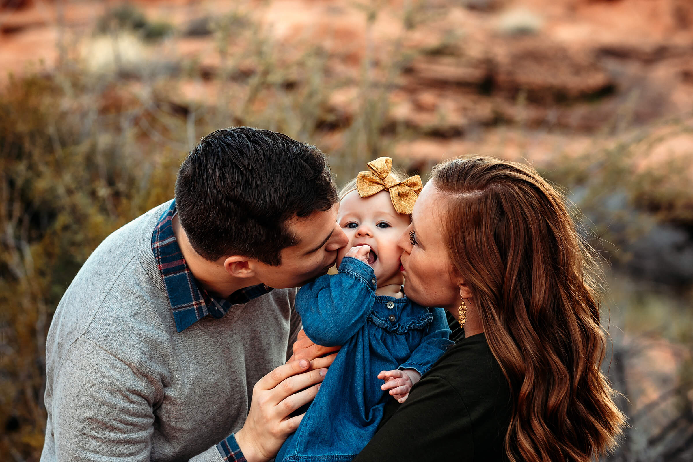 mom and dad kissing their daughter during a family session in Las Vegas