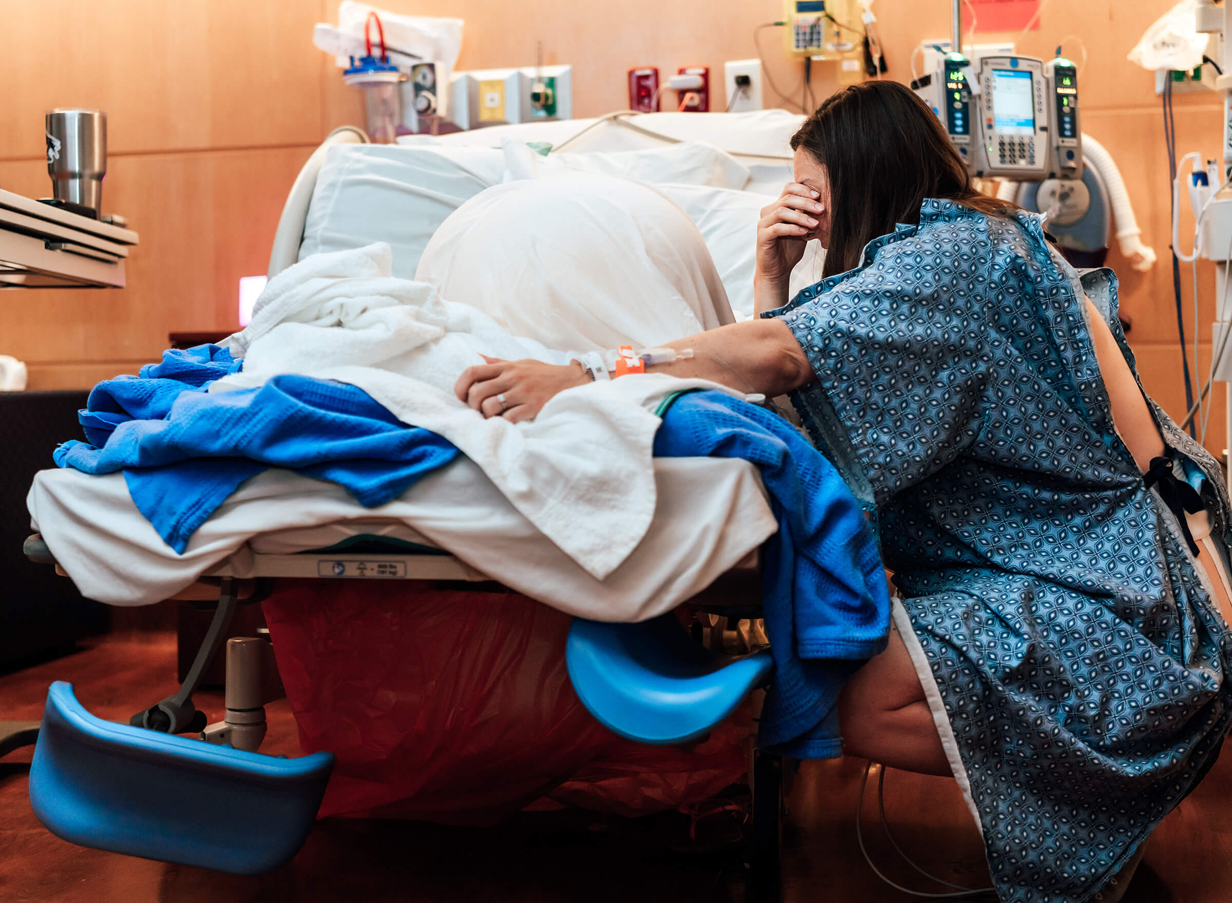 mother sitting on a birthing ball next to the bed for support while in labor