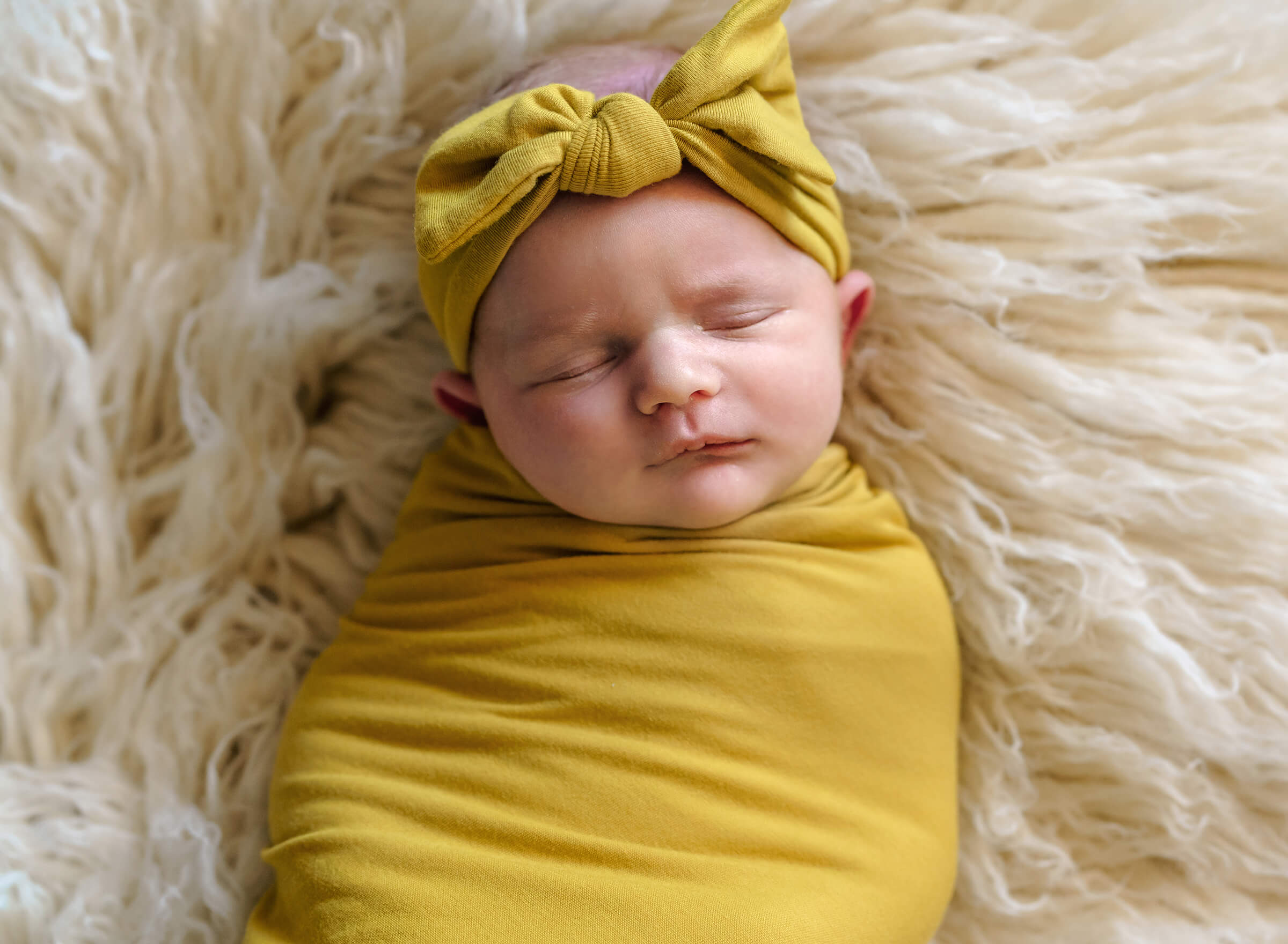 newborn swaddled in yellow wrap on ivory fur.