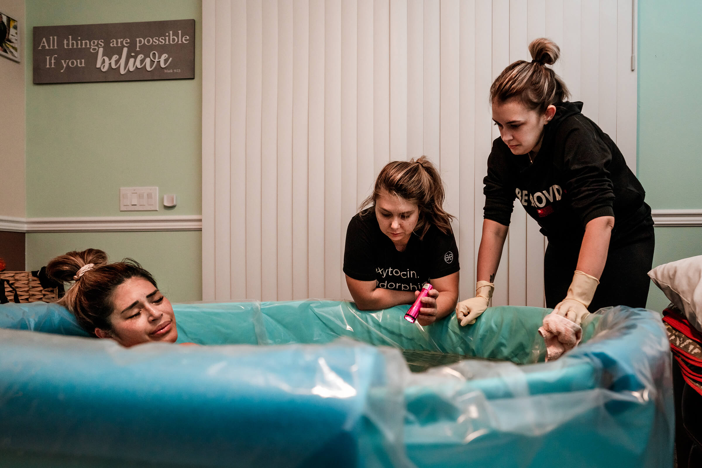 woman laboring in birth tub while doula and midwife watch