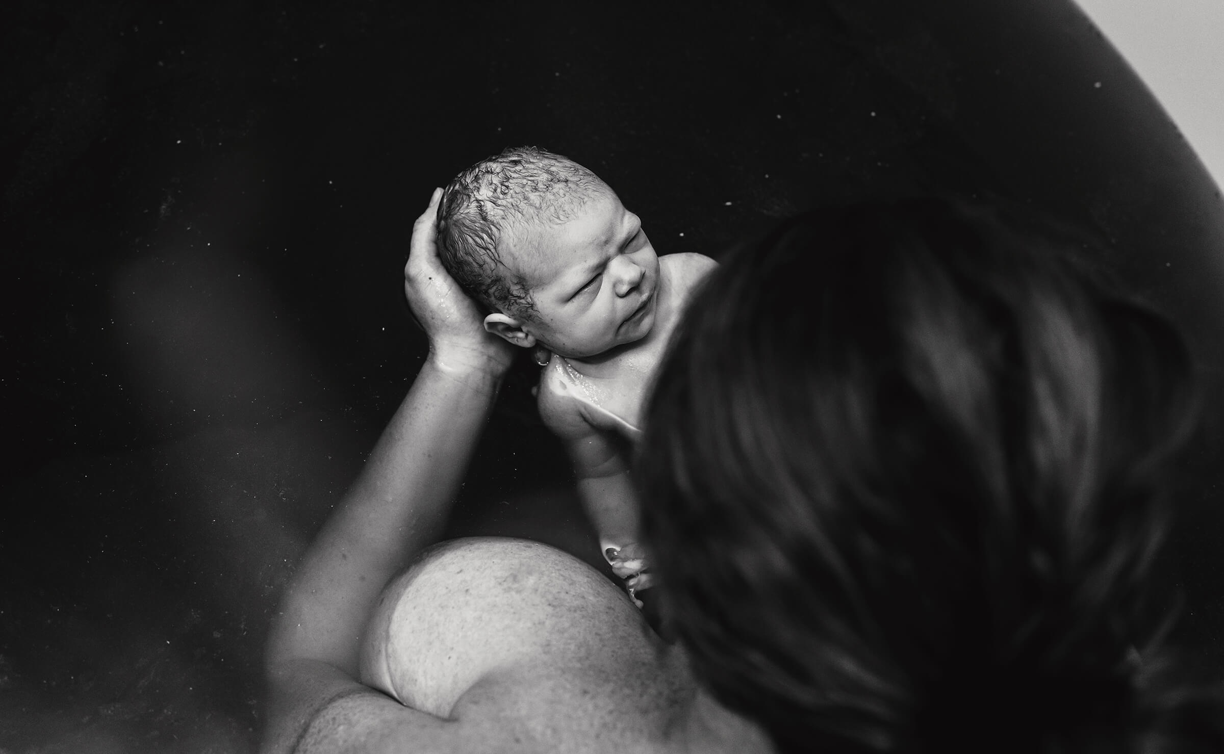 black and white image of a baby right after delivery in a birth tub. 