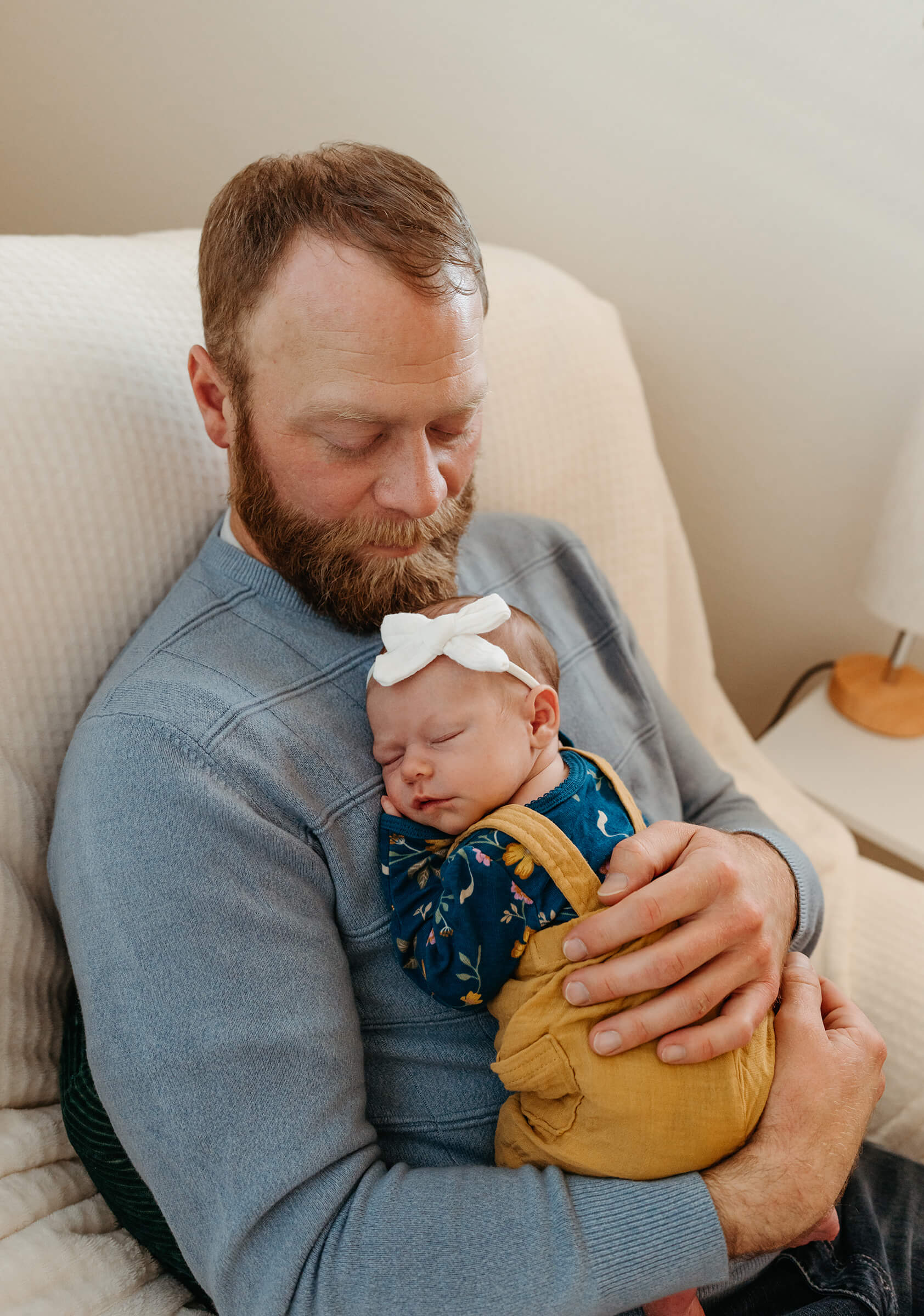 dad holding his newborn girl in a rocking chair during in-home newborn session. 