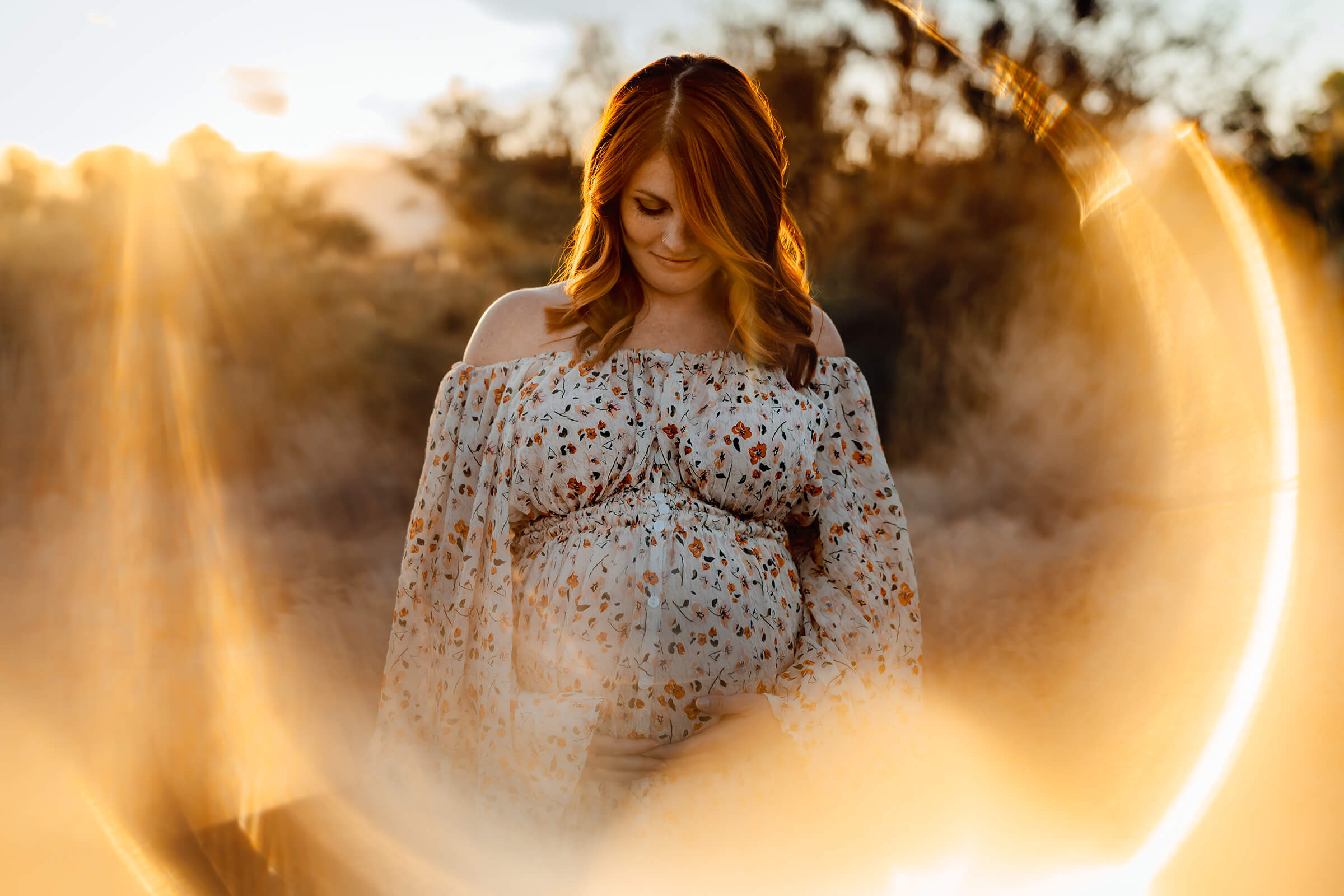 a maternity session in the desert using sun flare with mother holding her belly. 