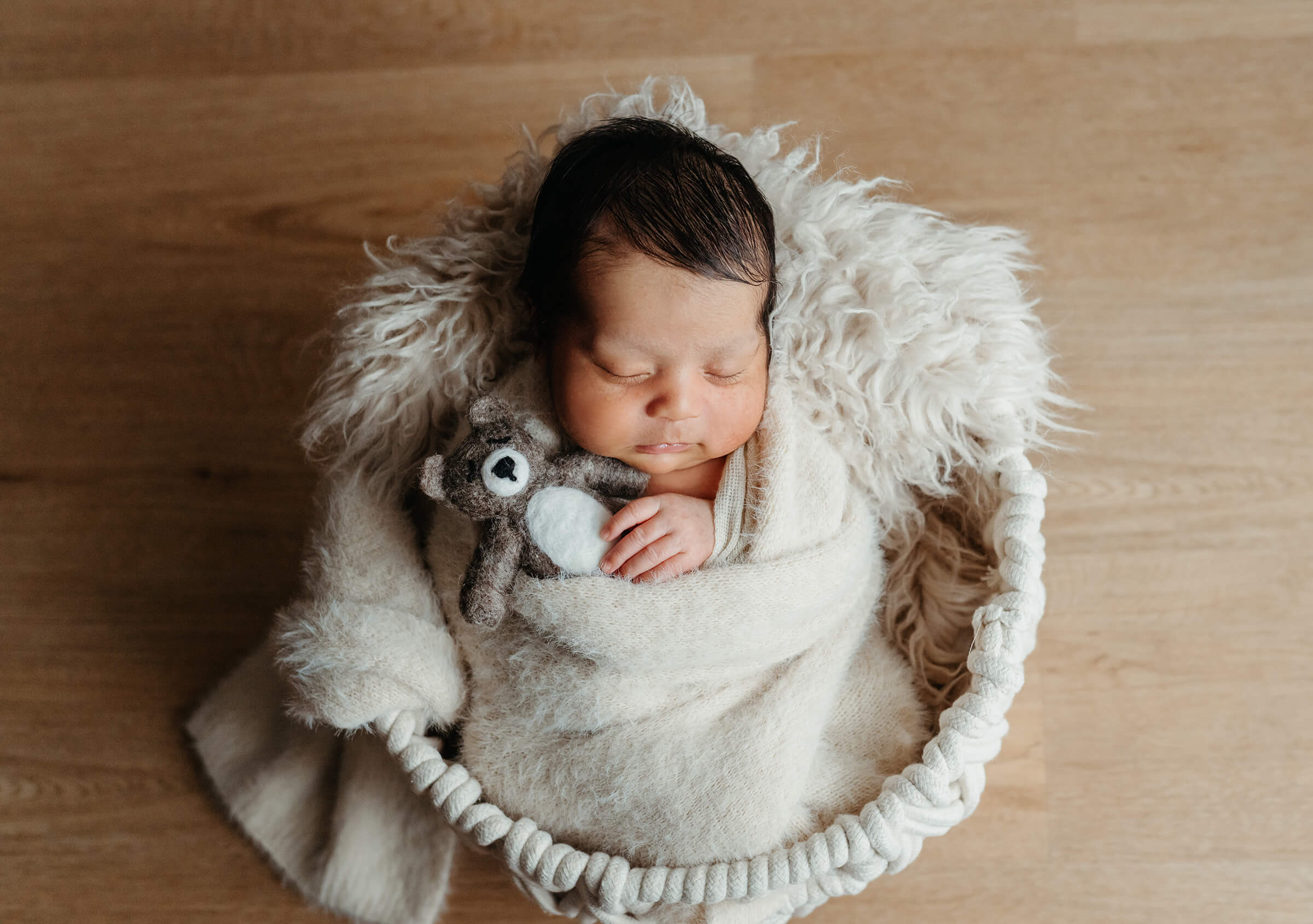 newborn in cream wrap holding small teddy bear