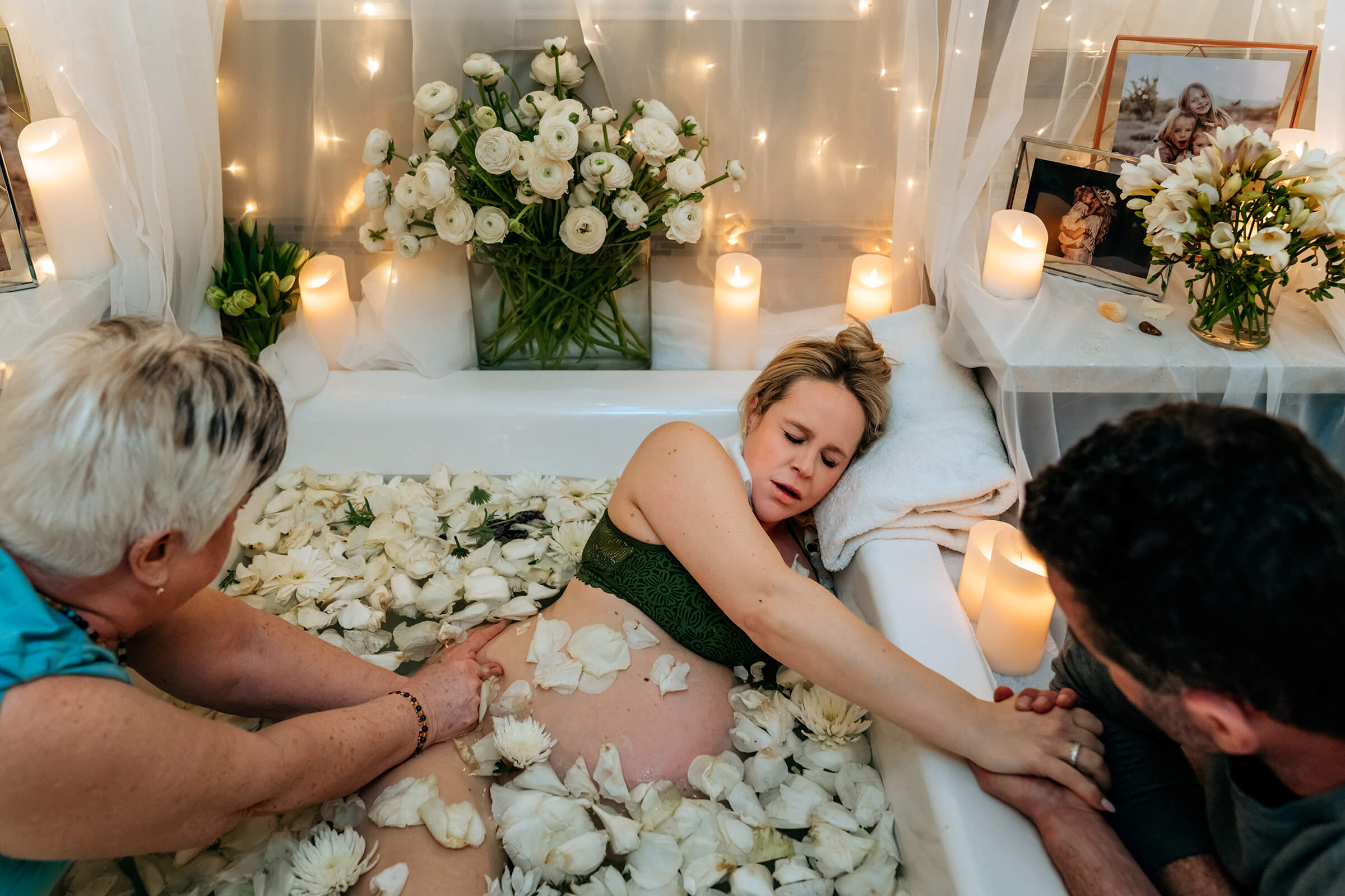 husband and doula physically supporting mother as she labors in tub wiht flower petals