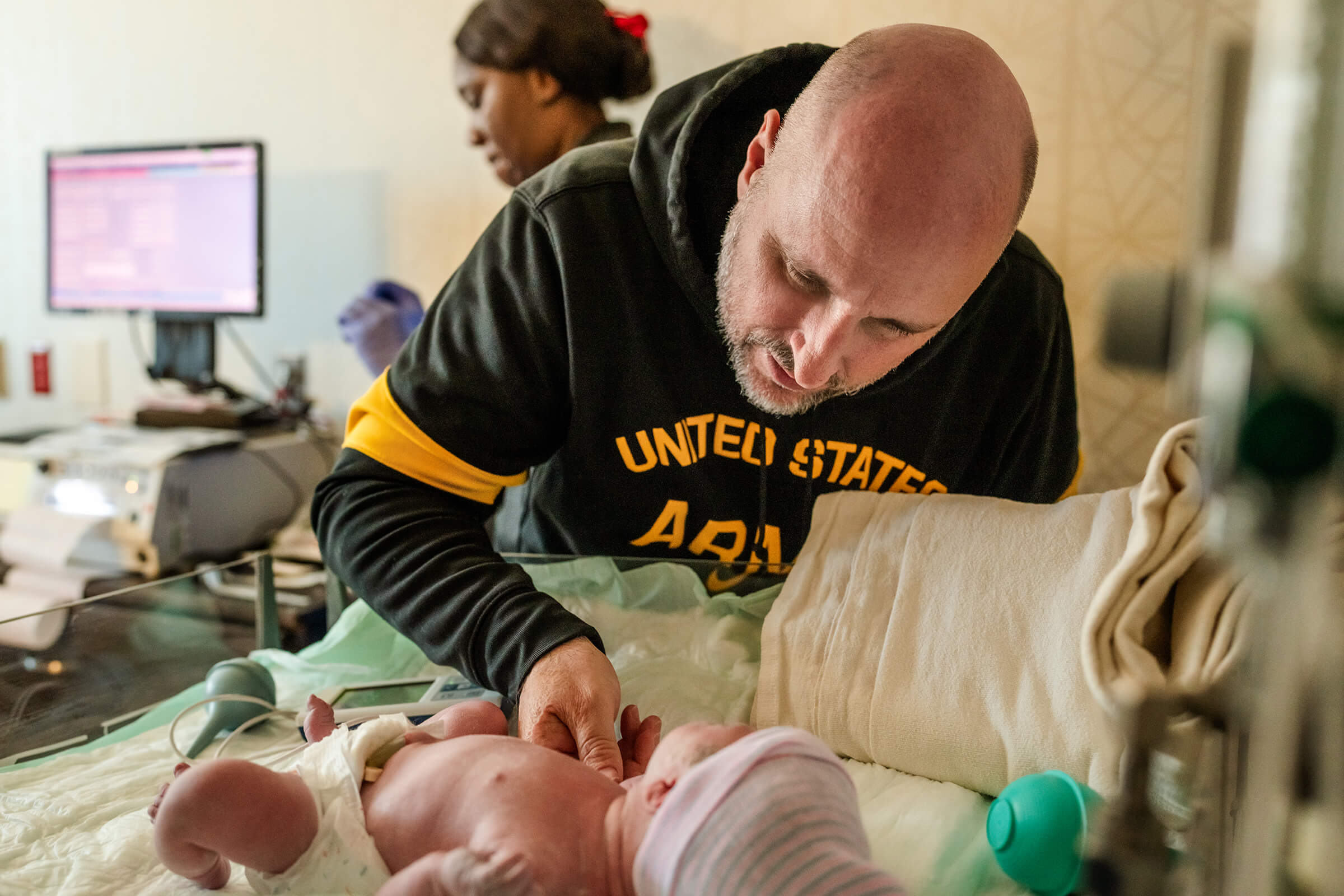 father holding his newborn daughter's hand while she's in the warmer after delivery