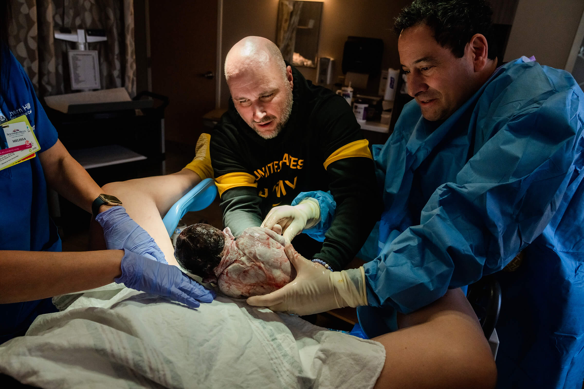 father delivering his own baby and placing on his wife's belly during a hospital delivery