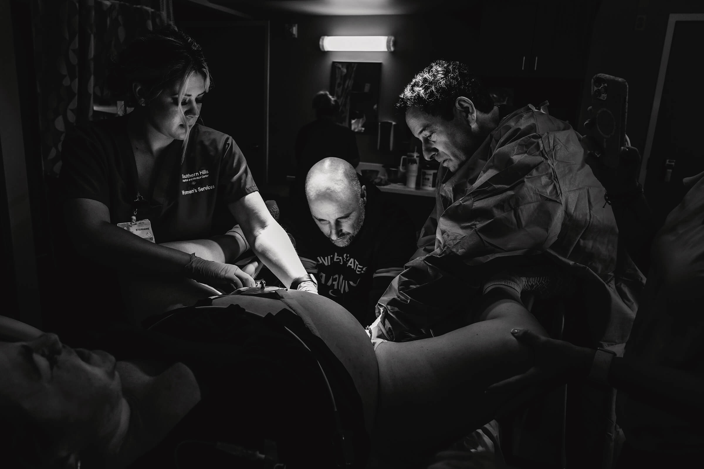 a black and white image of a father delivering his own baby in the hospital setting