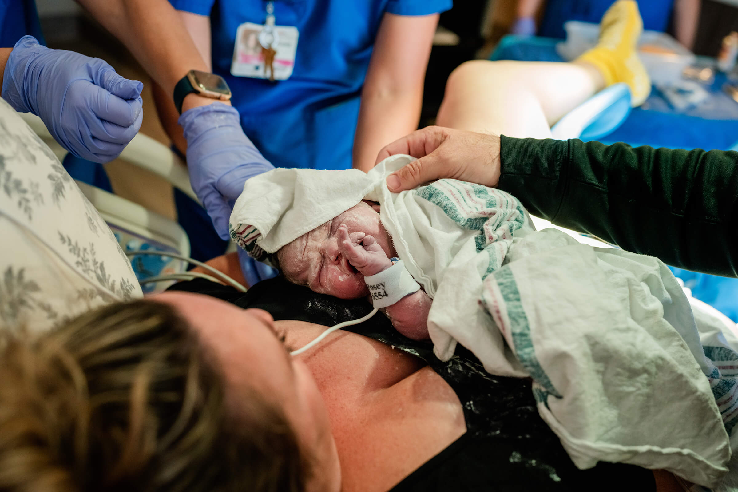 newborn baby being dried with a towel immediately after delivery while on mom's stomach