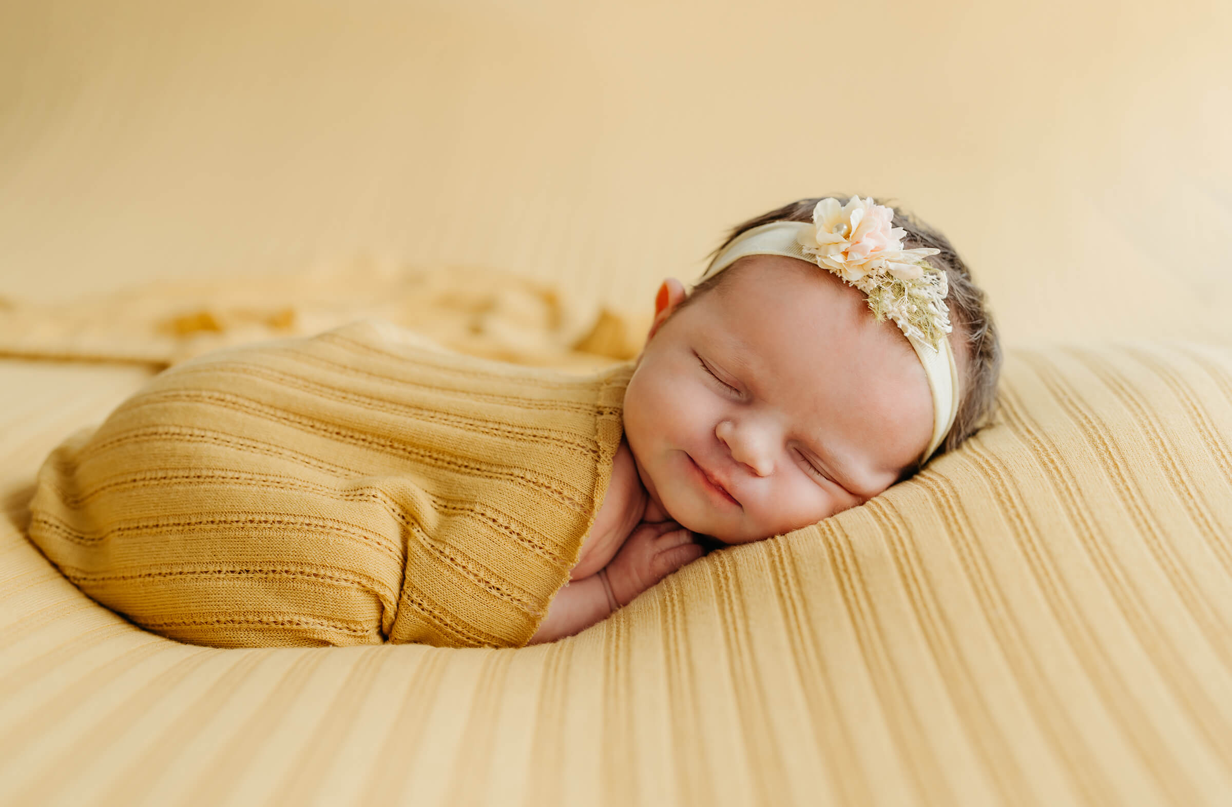 newborn posed on a yellow cloth while swaddled in a yellow wrap