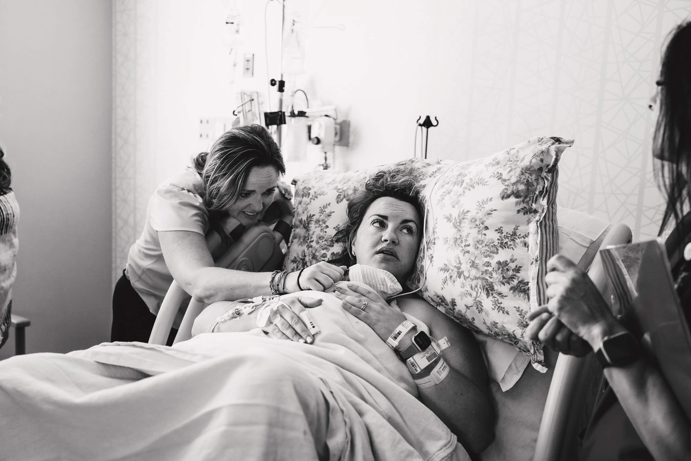 black and white image of a mother holding her new baby while her sister leans over the bed rail