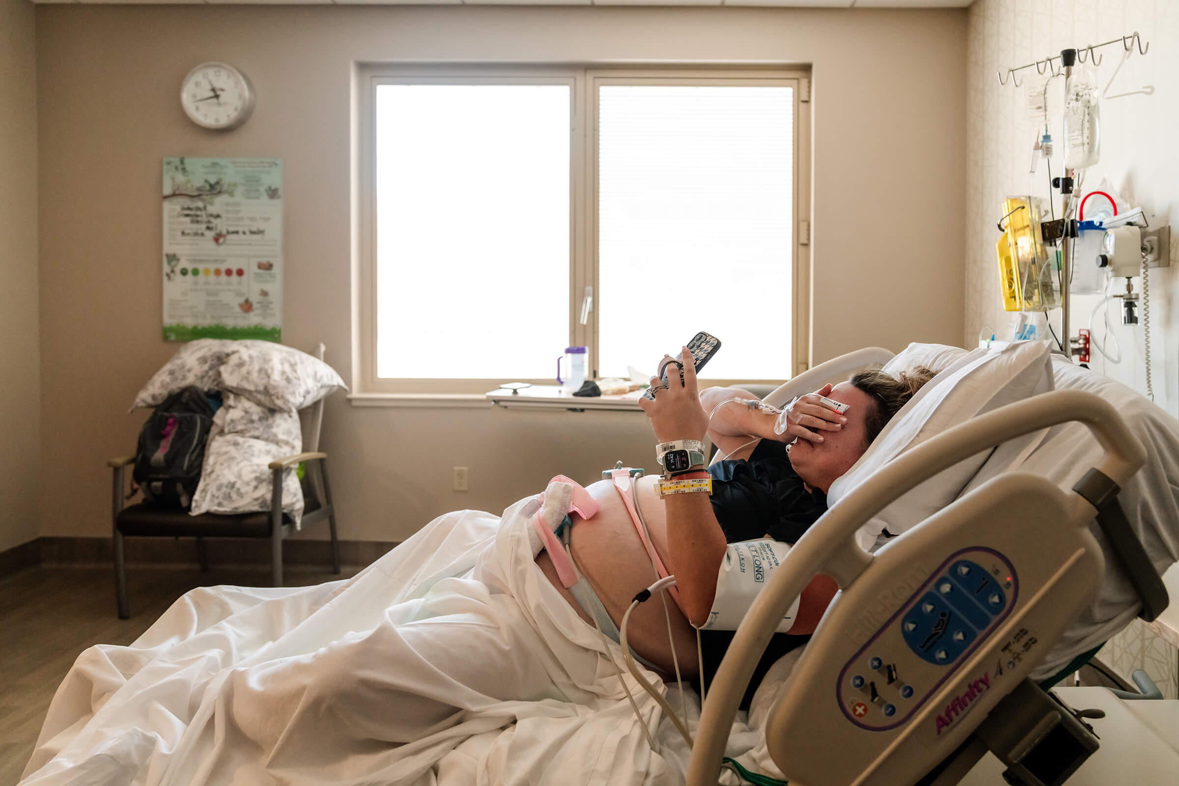 a pregnant woman in a hospital bed talking on the phone with her family while emotional