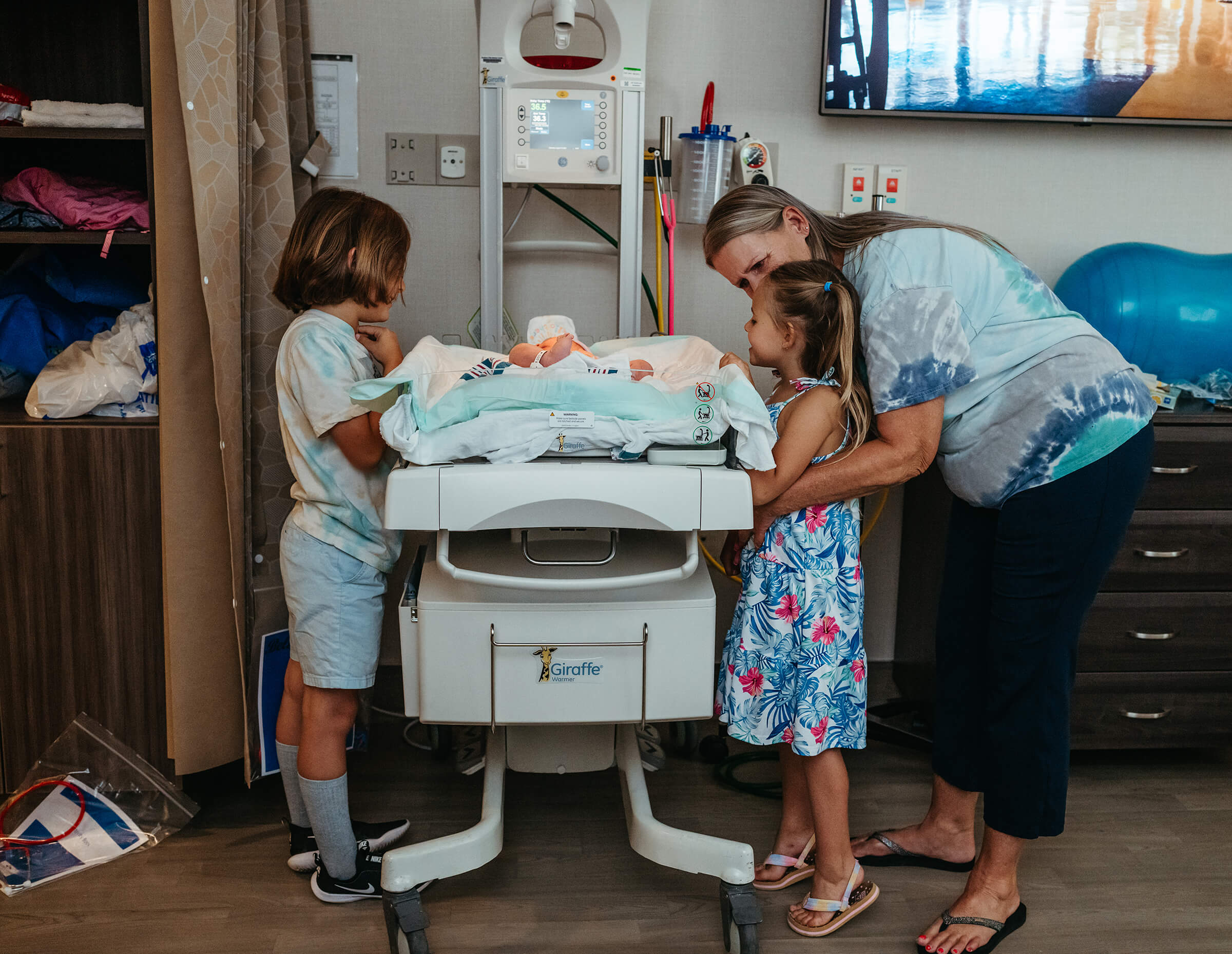 big brother and sister along with grandmother looking at their new baby brother after a hospital delivery