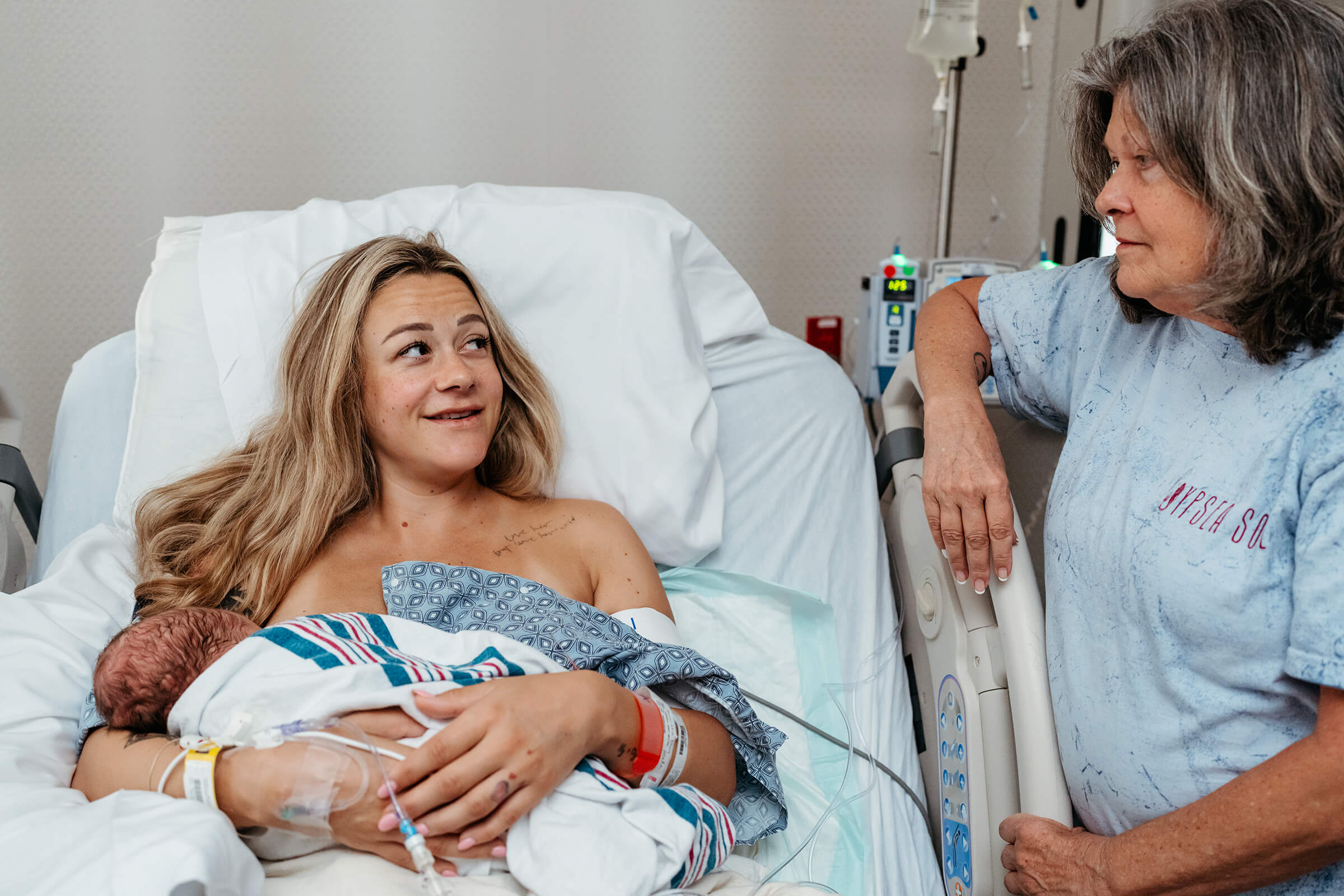 grandmother at the bedside of her daughter as she holds her new infant after delivery