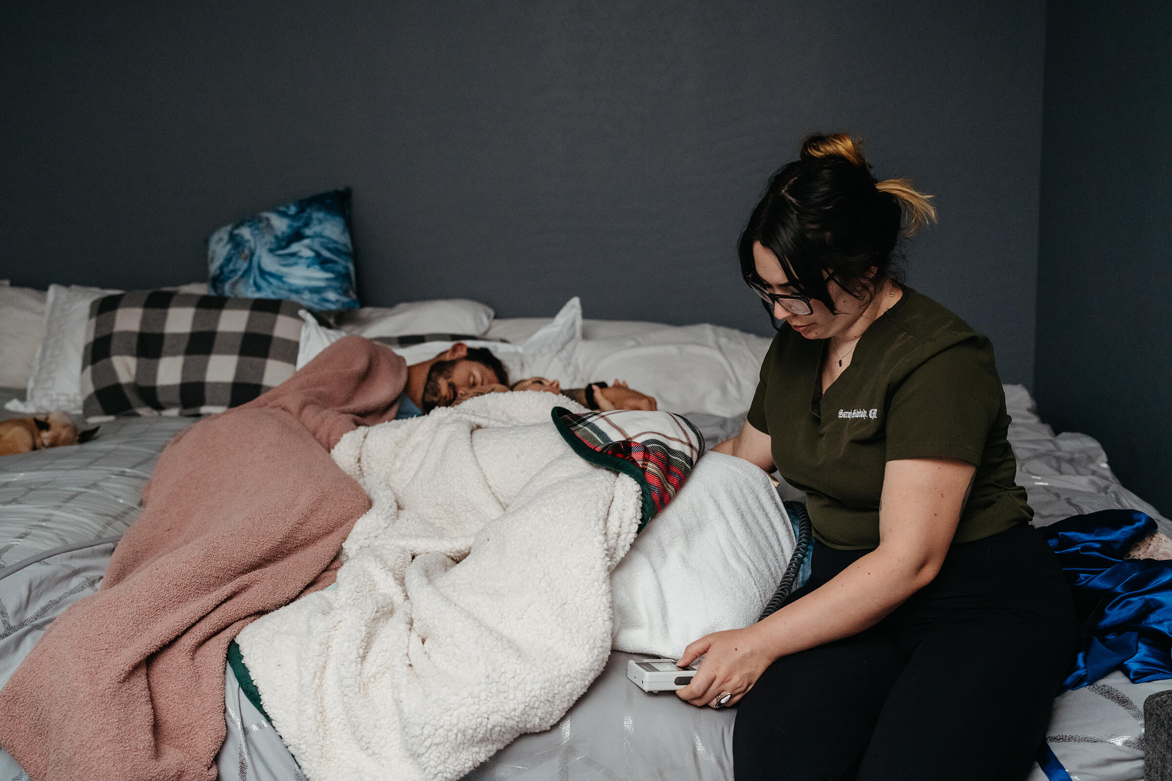 parents resting while in labor with lights dimmed and midwife by their side