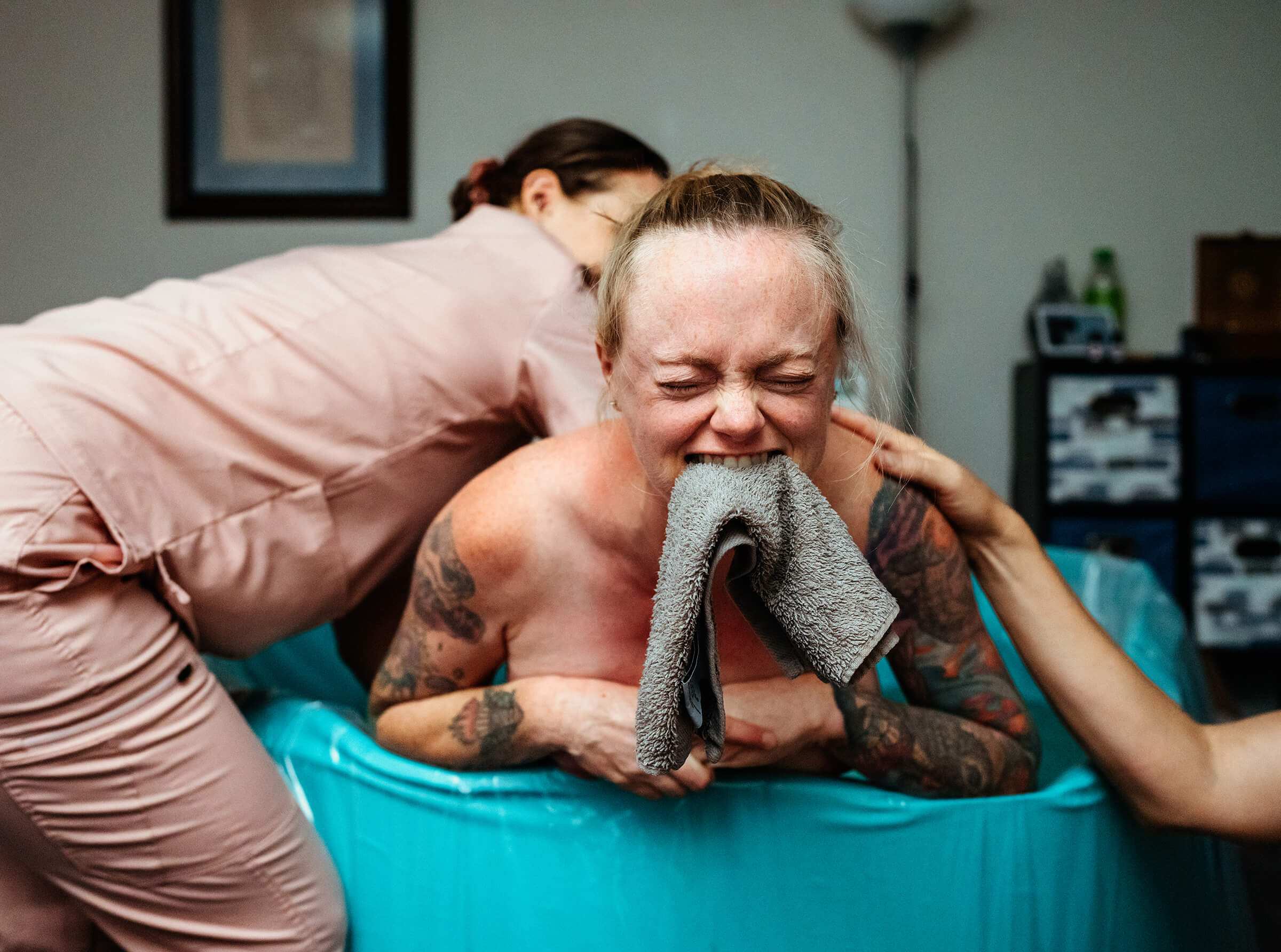 image of doula rubbing lower back of a woman in labor as she bites a washcloth