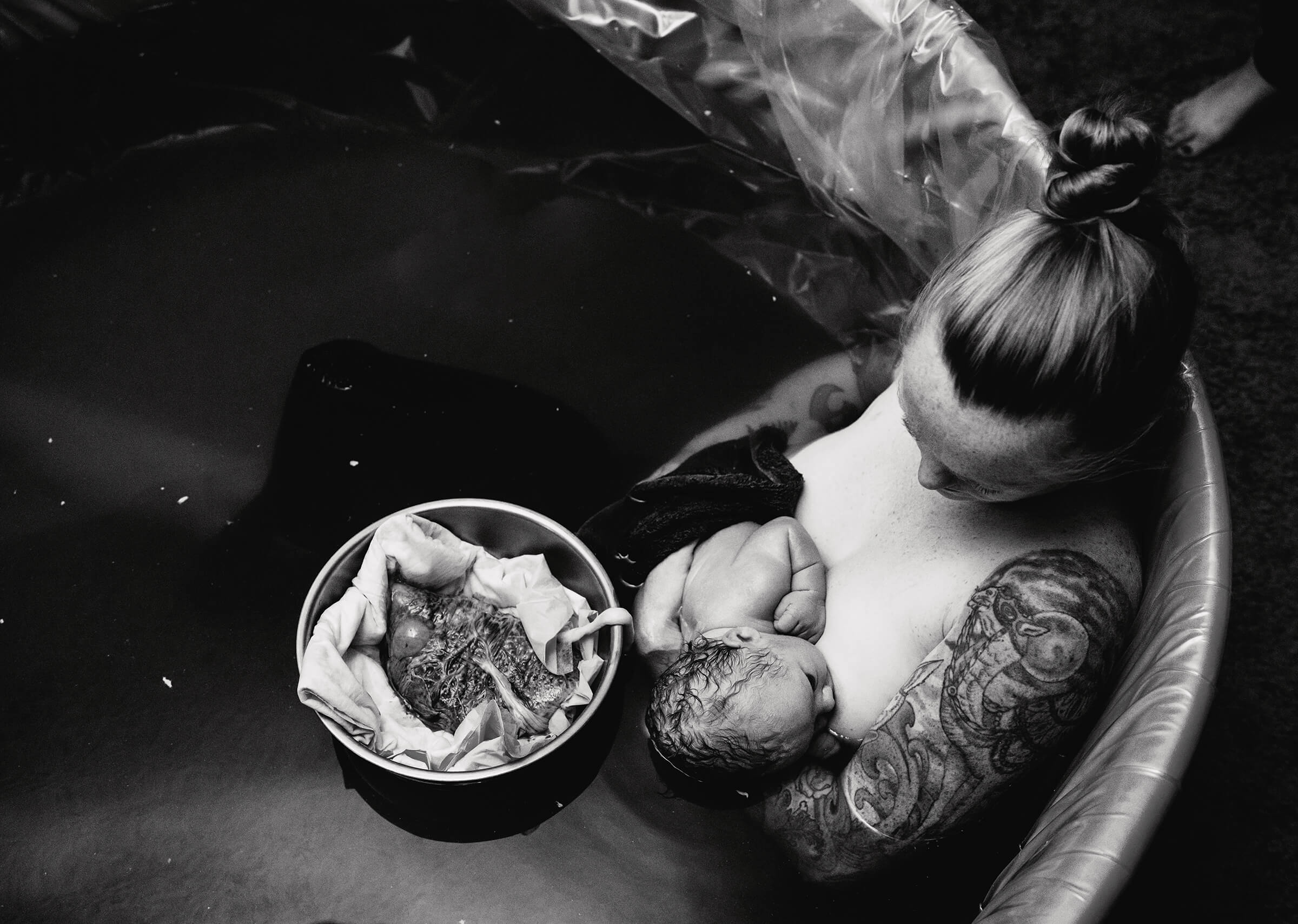 black and white image of woman in birth tub with placenta still attached to her baby