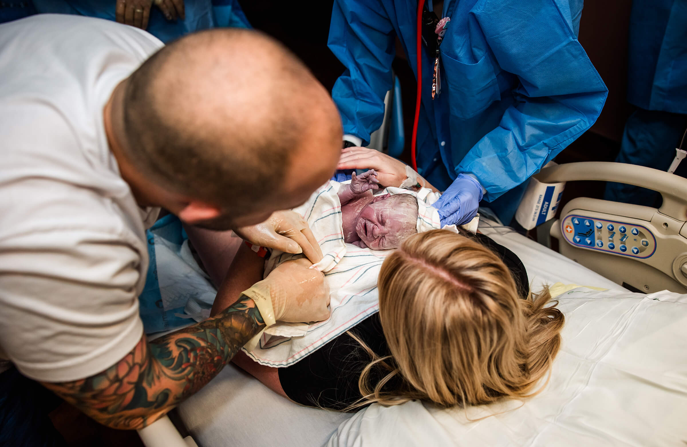 An aerial perspective of a newborn baby on mom's chest with both parents looking at baby.