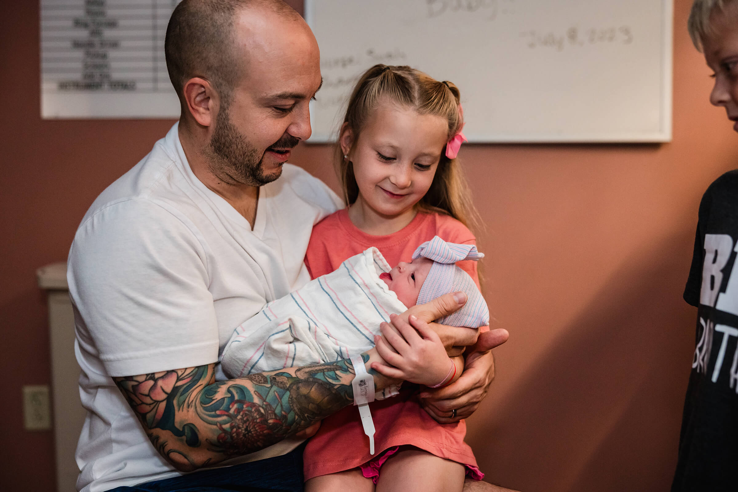 big sister holding her new baby sister on her lap while dad supports them both.