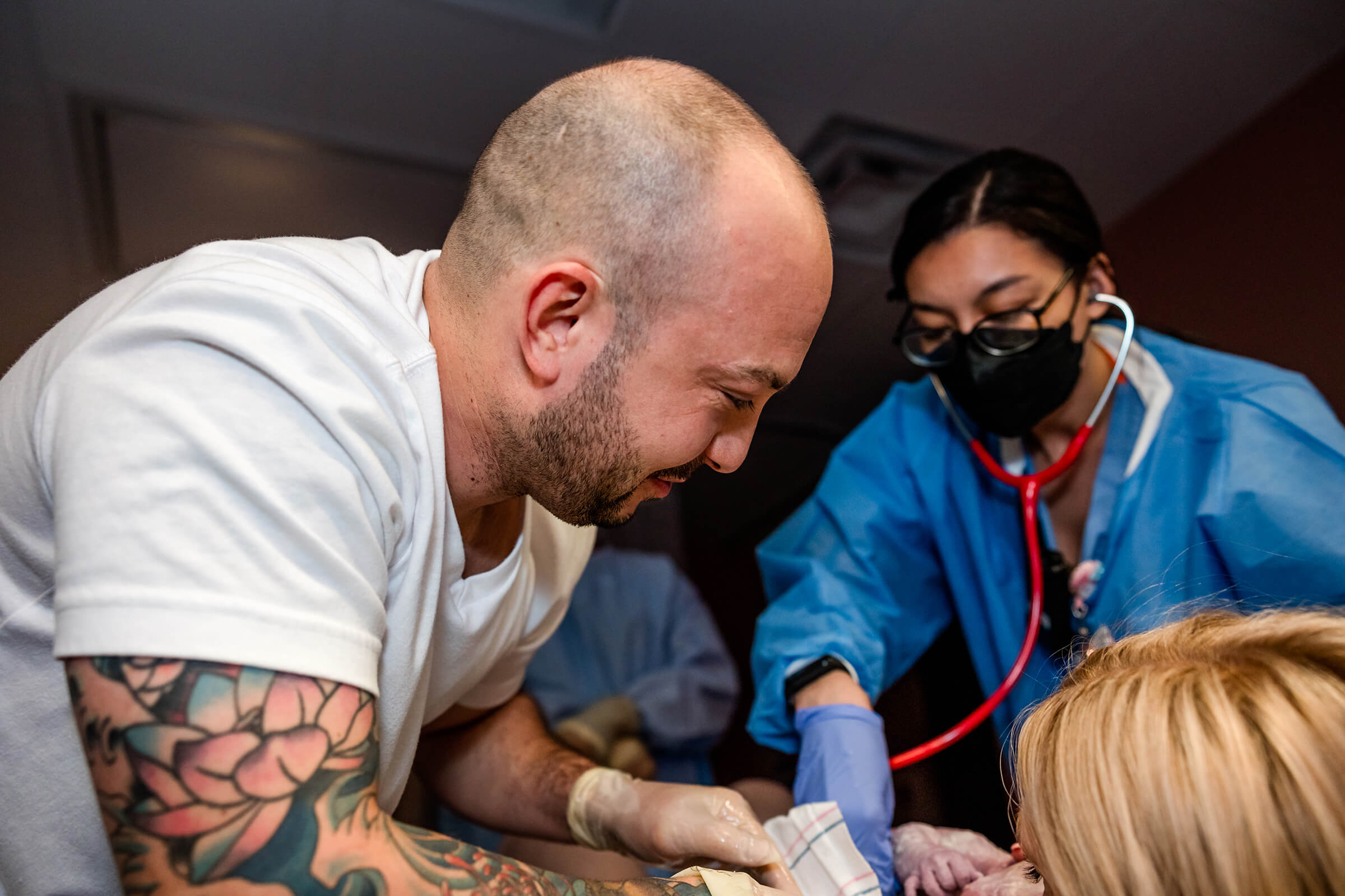 a side view of a dad with tears of joy seeing his daughter being born in a Las Vegas hospital.