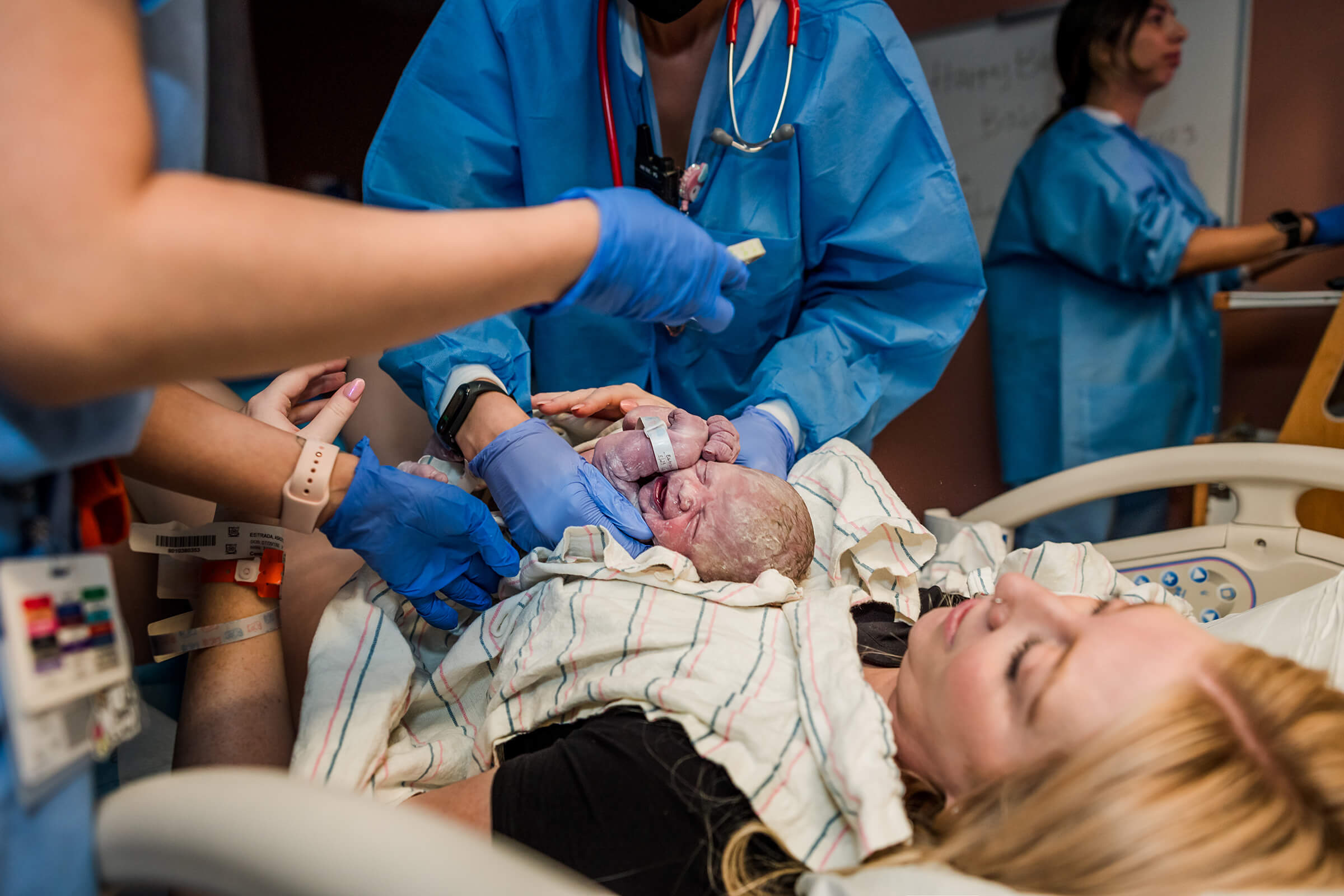 a nurse stimulating and drying off a new baby immediately following birth while baby is still on mom's stomach.