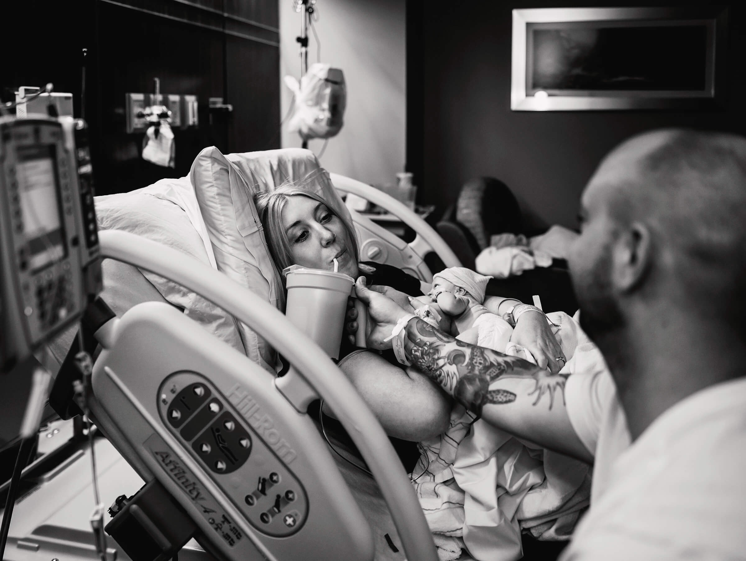 mother drinking water held by dad while breastfeeding after a hospital birth.