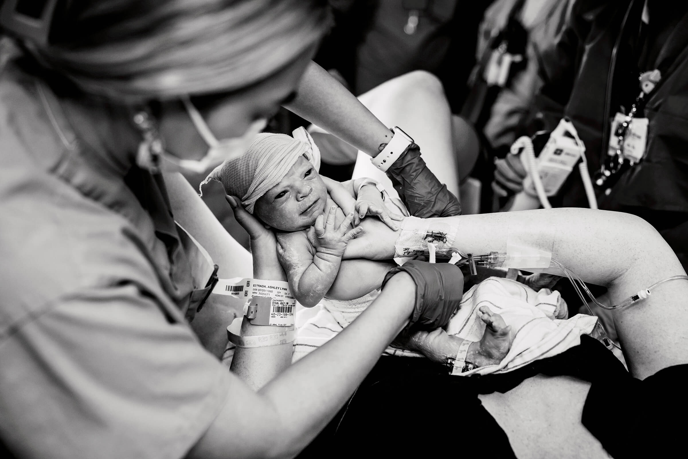 a black and white image of a mother holding her new baby on her chest while she looks at her face.