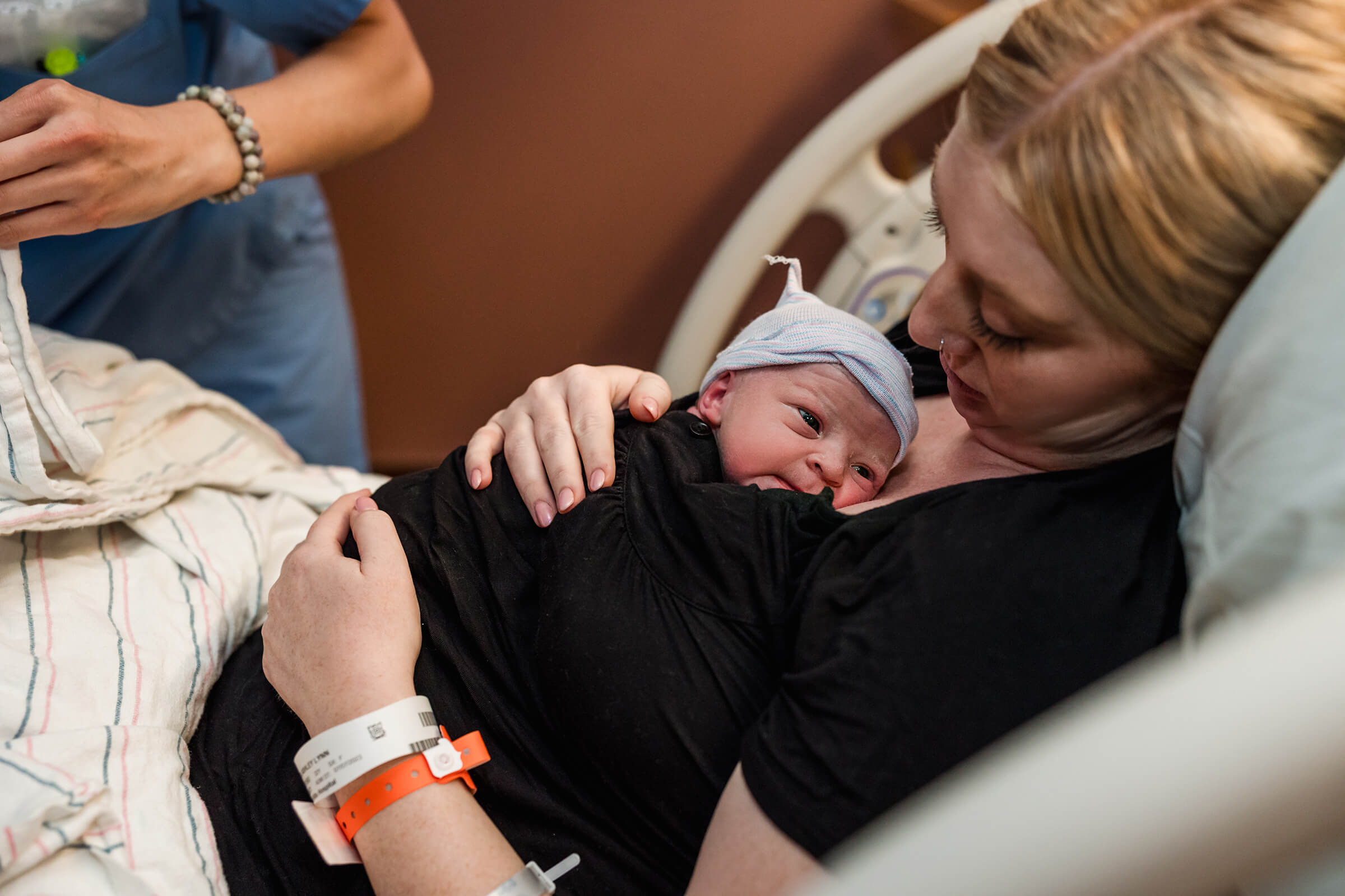 mother holding her infant skin-to-skin in her hospital bed after delivery.