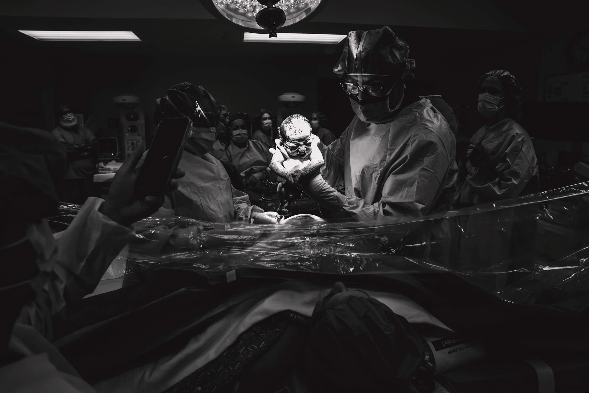 black and white dramatic image of twin B being lifted above clear drape for parents to see