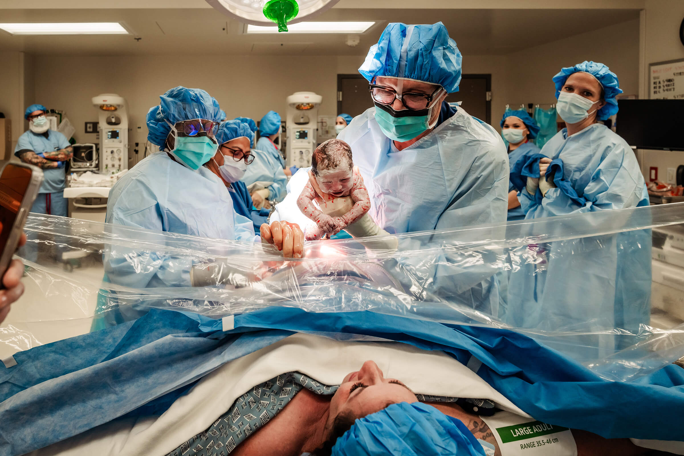 Doctor lifting baby over clear drape for parents to see in the operating room